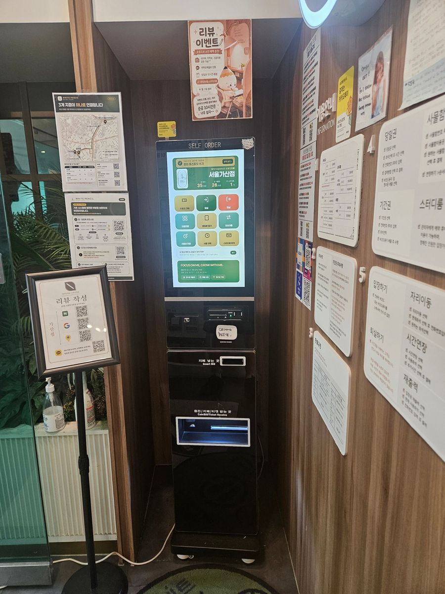 서울가산점 입구에 서 있는 구형 키오스크. 화면에 새 첫 화면이 떠 있고 아래에 카드 단말과 지폐 투입구가 있습니다.